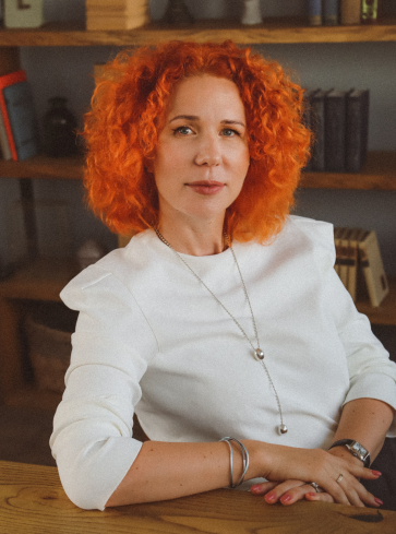 A woman with red hair sitting in front of some books