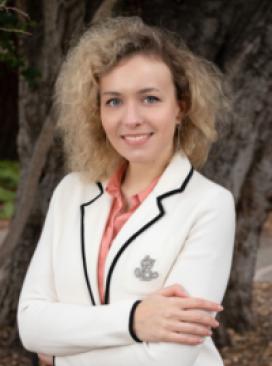 A woman in white jacket standing next to tree.