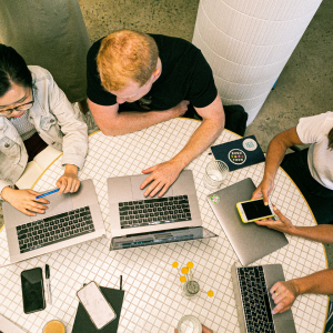 A group of people sitting around a table with laptops.